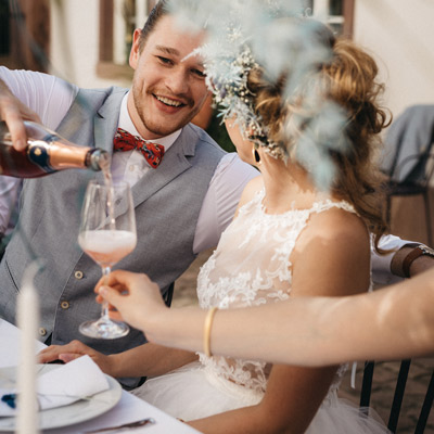 Zur Hochzeit gibt es Champagner- Der Bräutigam im weißen Hemd und hellblauer Weste mit roter Fliege